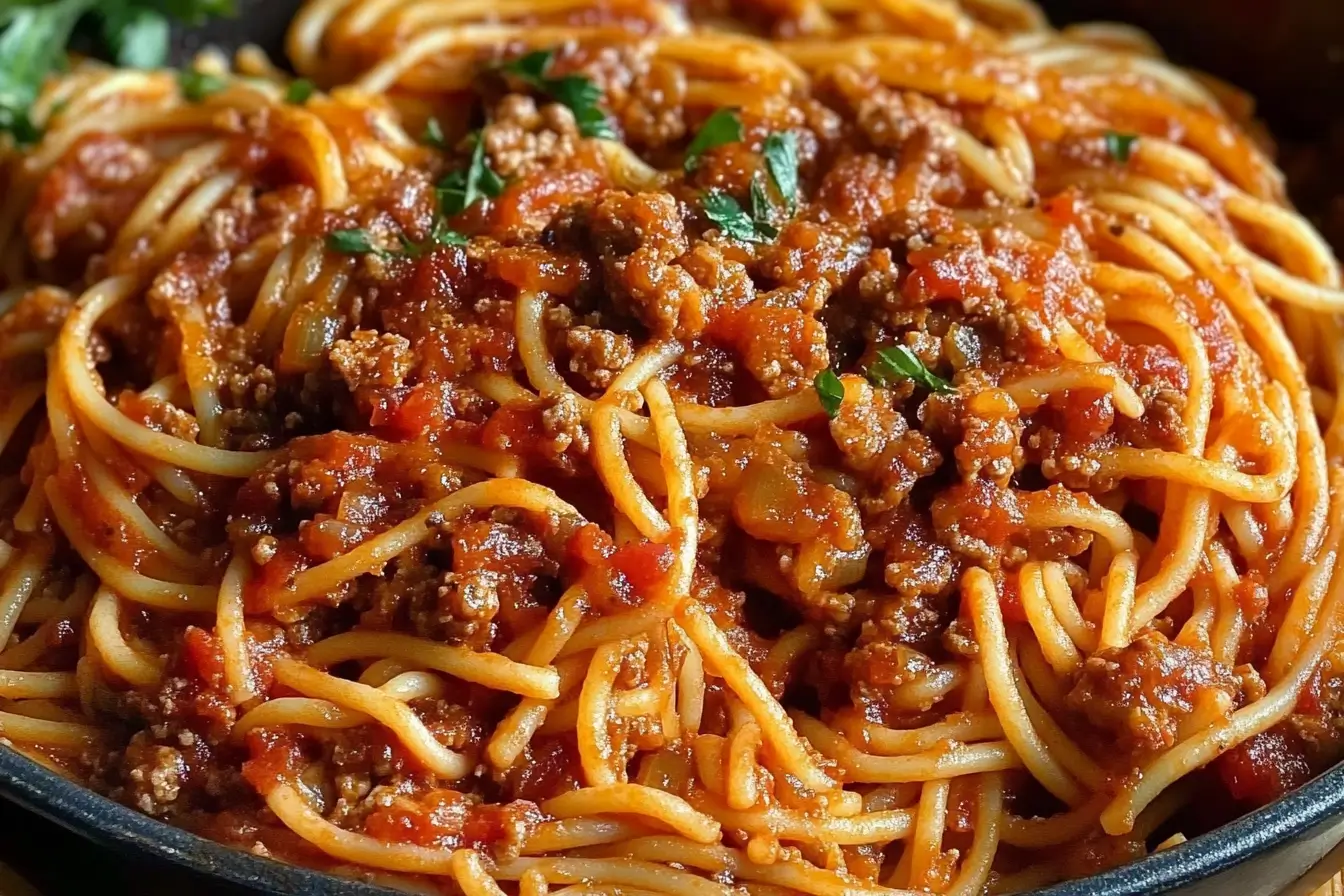Close-up view of delicious Old Fashioned Spaghetti topped with rich tomato meat sauce and garnished with fresh herbs.
